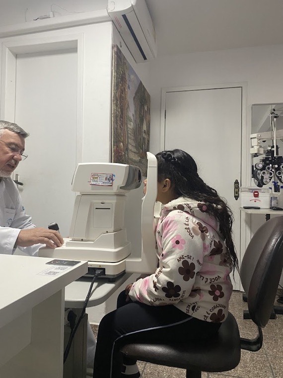Criança realizando exame de vista no equipamento, acompanhada pelo optometrista