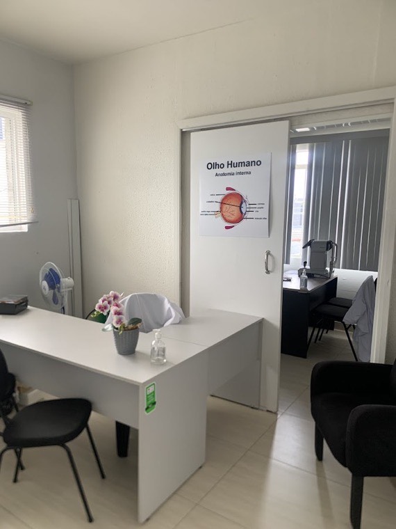 Recepção do consultório, com mesa de atendimento e sala de exames ao fundo